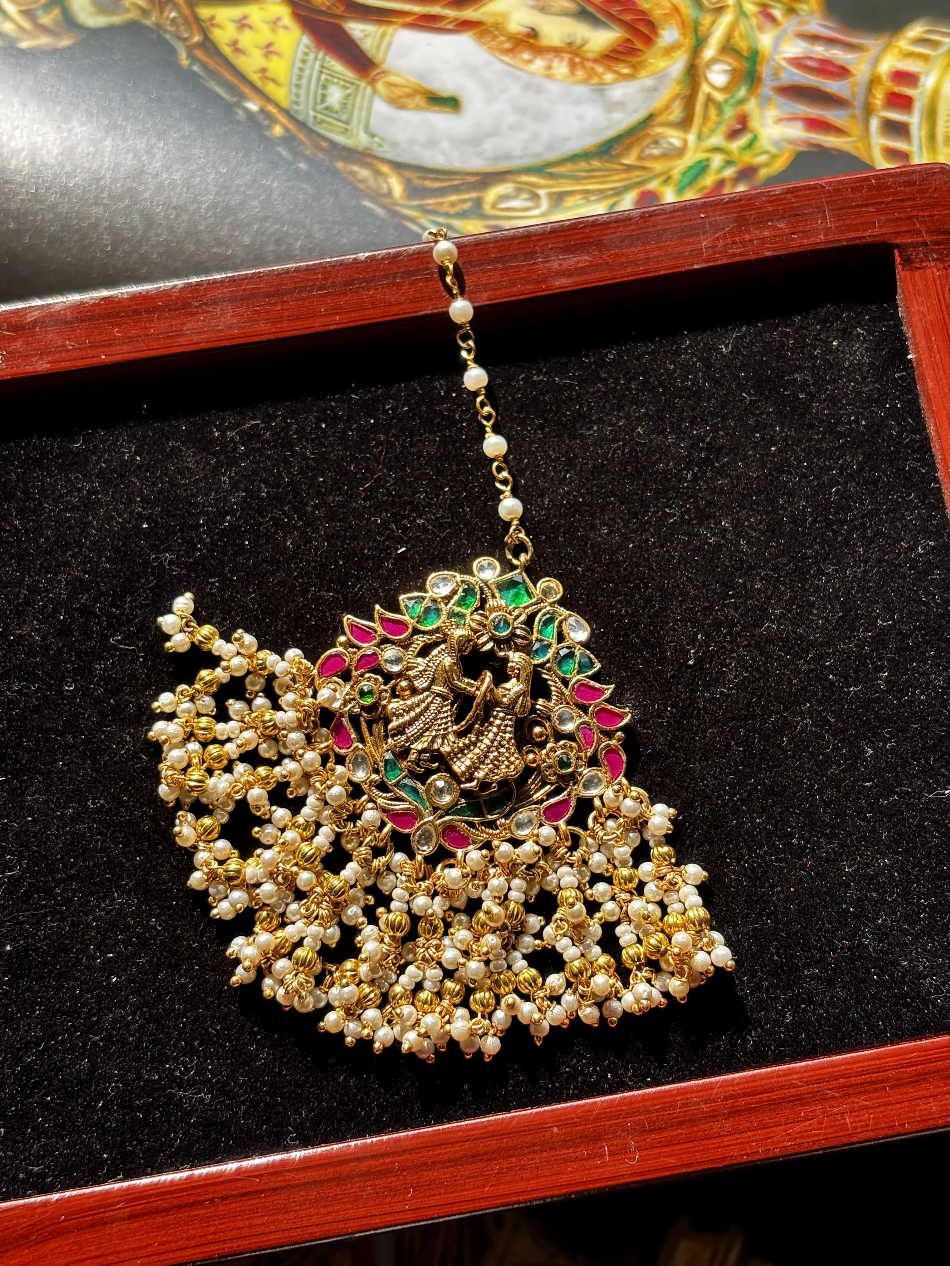Decorative gold maangtikka with pearls and gemstones on a black background