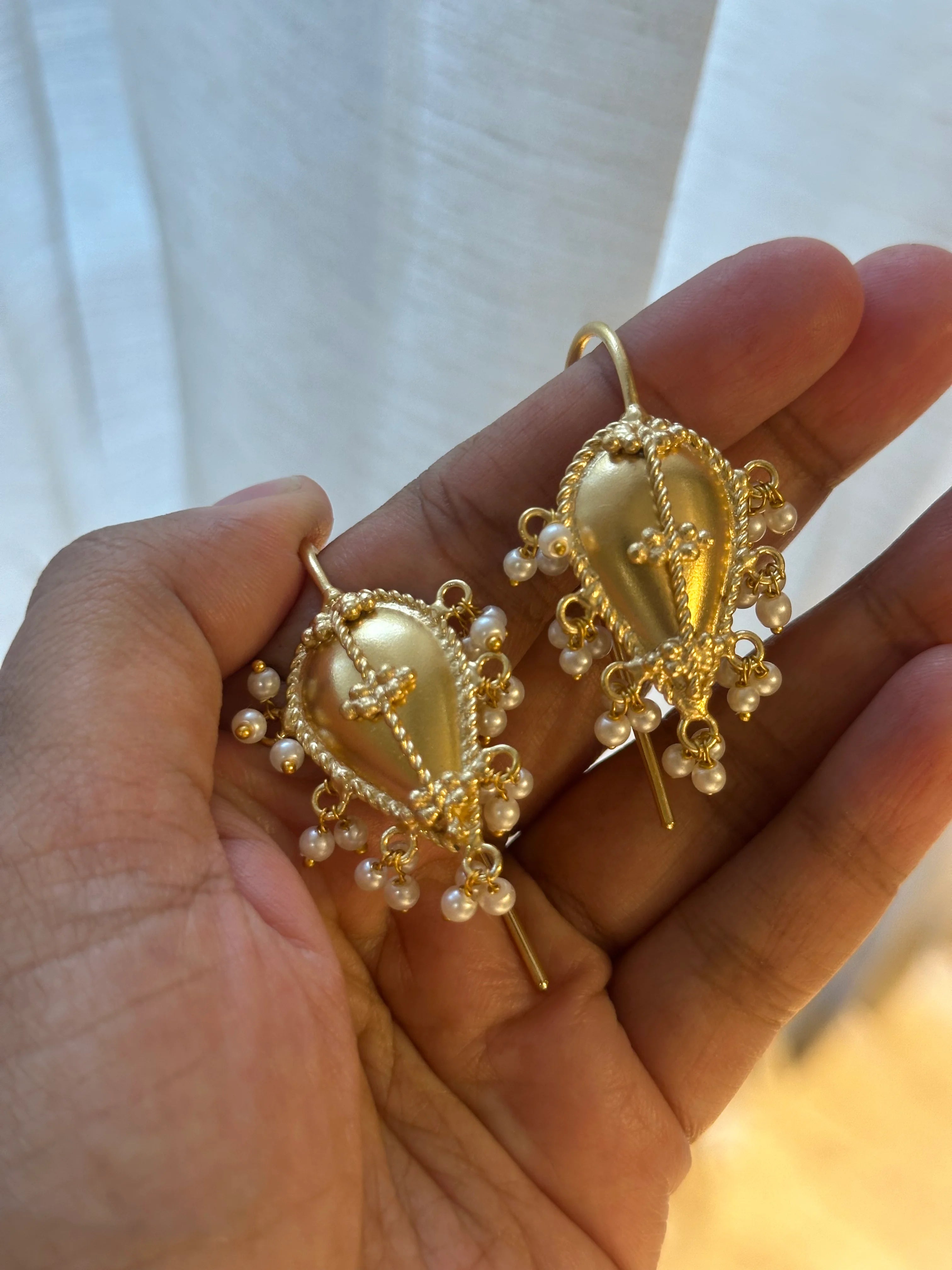 Gold earrings with pearl accents held in a hand against a white background