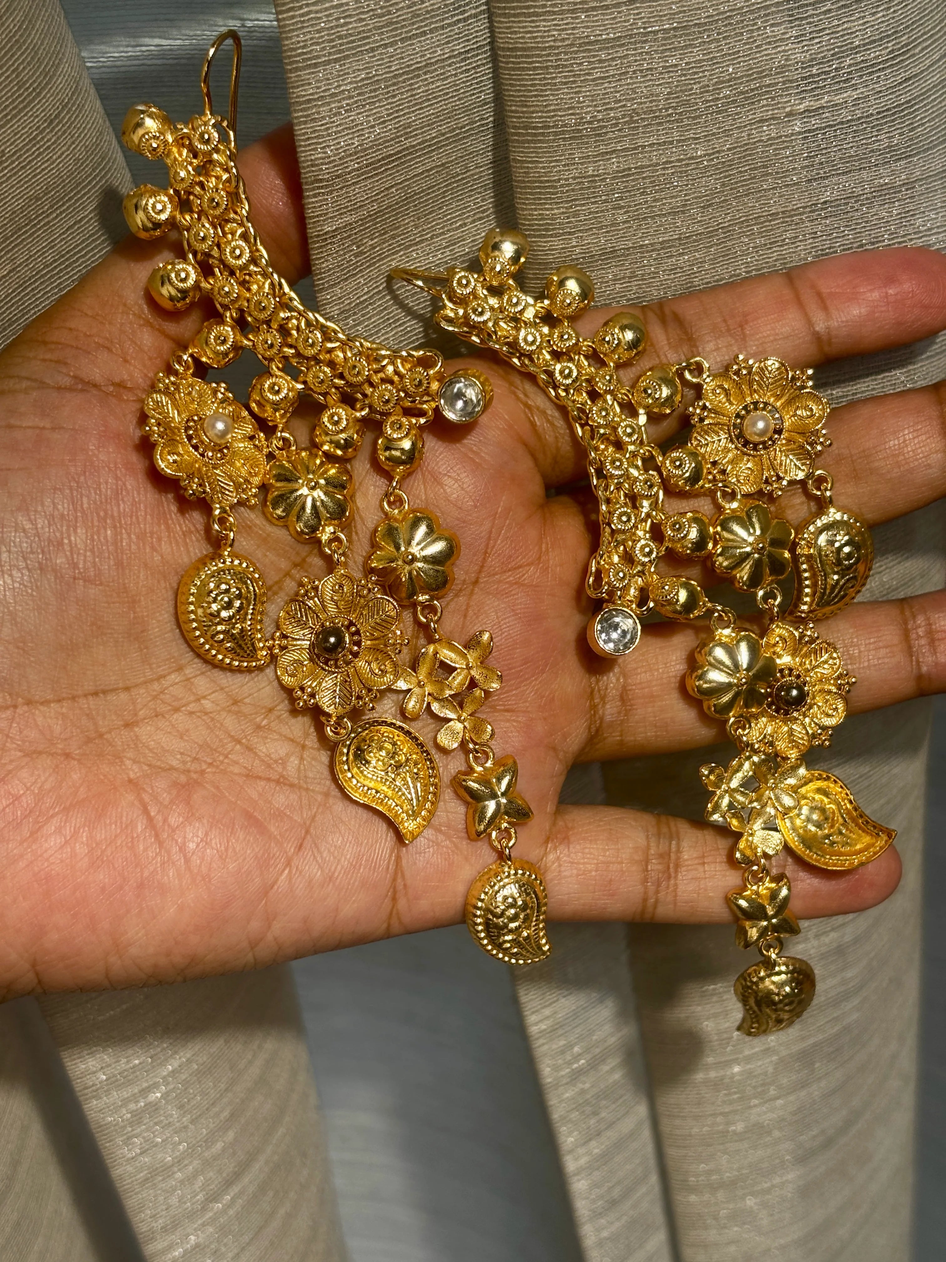 Gold jewelry set with earrings and bracelet on a hand against a neutral background