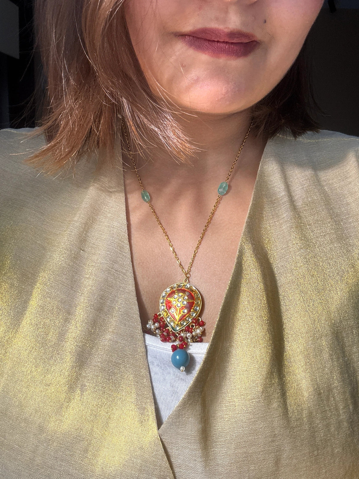 Close-up of a person wearing a colorful brooch and necklace with a neutral background