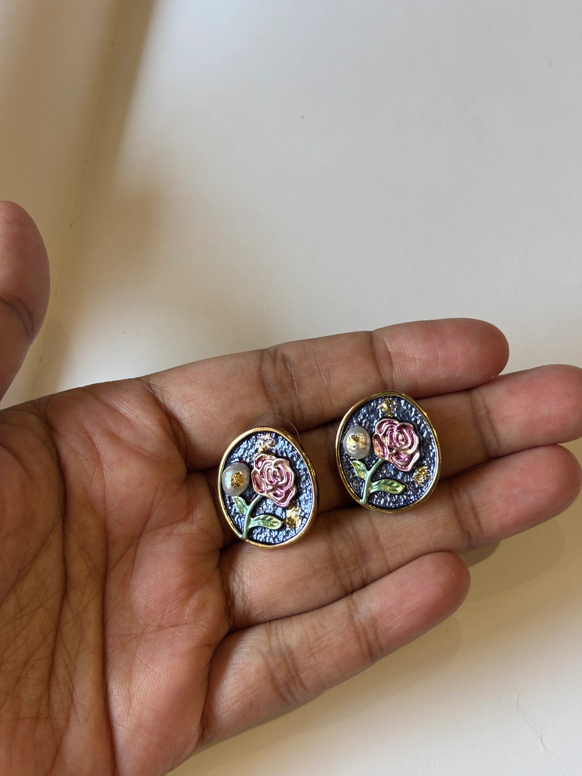 Two round floral earrings held in a hand against a plain background