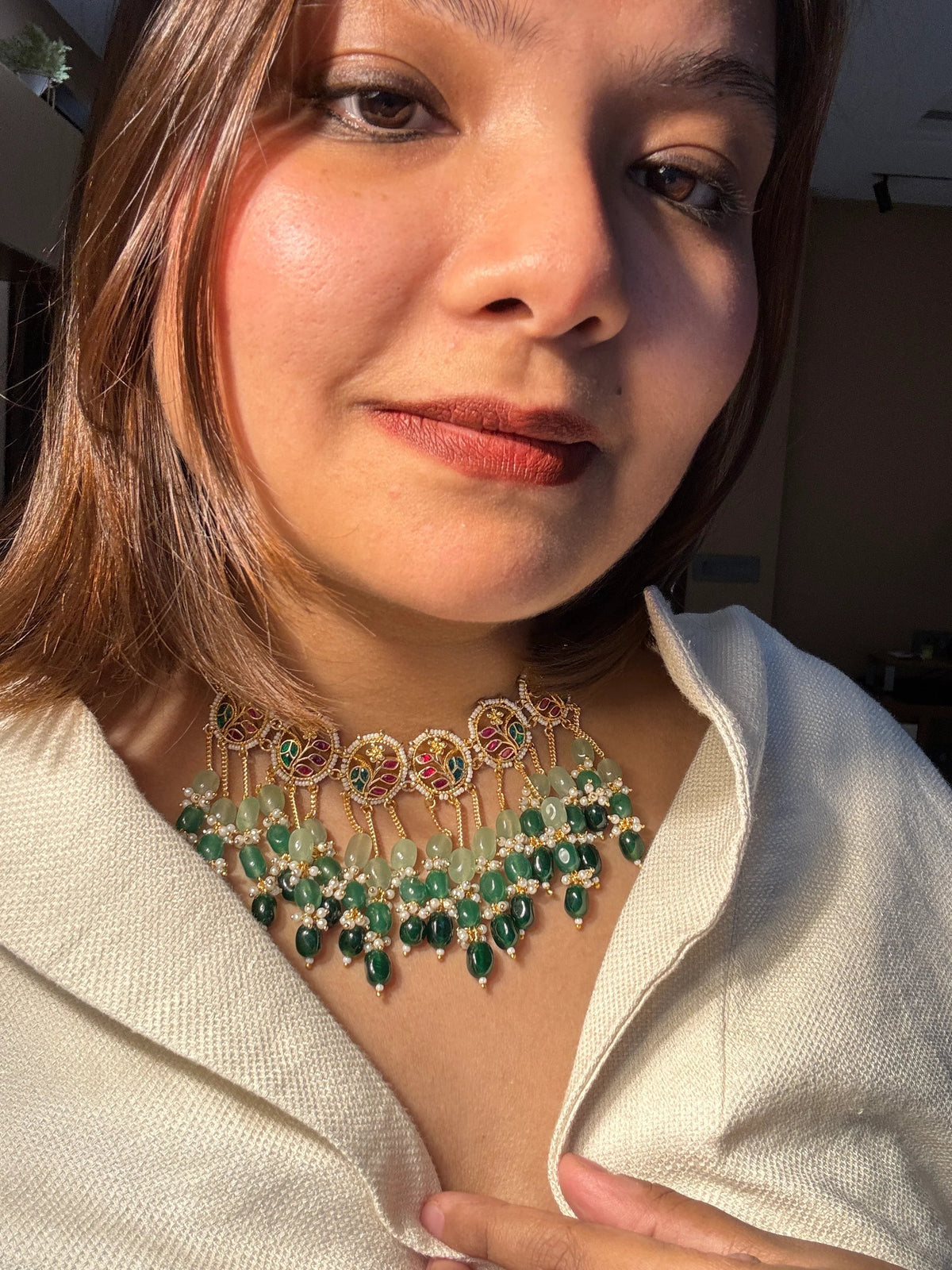Close-up of a woman wearing a decorative necklace with green gemstones.